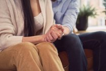 Багаторасова пара сидить на дивані в офісі психолога і тримає руки під час призначення психотерапії — стокове фото