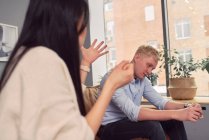 Unhappy Asian woman taking to indifferent man during therapy session in office of psychologist — Stock Photo