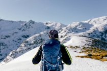 Vista posteriore dell'alpinista maschio irriconoscibile in caldo activewear con zaino in piedi sul pendio della montagna rocciosa innevata e godendo di uno spettacolare paesaggio nella soleggiata giornata invernale — Foto stock