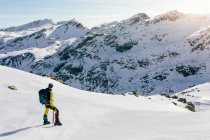 Vue arrière du corps complet de l'alpiniste masculin méconnaissable en vêtements de sport chauds avec sac à dos debout sur la pente de la montagne rocheuse enneigée et profiter d'un paysage spectaculaire dans la journée ensoleillée d'hiver — Photo de stock