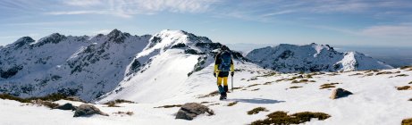 Visão traseira do escalador irreconhecível andando na encosta da neve coberto cordilheira rochosa em tempo ensolarado — Fotografia de Stock