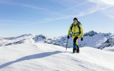 Male climber in outwear walking on slope of snow covered rocky mountain range in sunny weather — Stock Photo