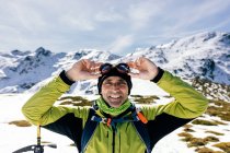Впевнений щасливий чоловік альпініст у стильному теплому активному одязі з рюкзаком обладнання для скелелазіння, що стоїть на вершині гори і дивиться на камеру, досліджуючи сніговий скелястий пейзаж у сонячну погоду — стокове фото