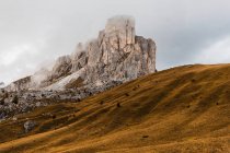 Picturesque scenery with rough steep rocky peak and hills covered with yellow grass under clouds in Dolomites mountain range in Italy — Stock Photo