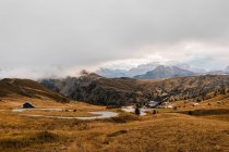 Pintoresco paisaje con áspero pico rocoso empinado y colinas cubiertas de hierba amarilla bajo las nubes en la cordillera de los Dolomitas en Italia - foto de stock