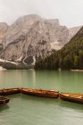 Деревянные лодки пришвартованы в спокойной зеленой воде озера в окружении величественных скал и лесистых холмов в горном массиве Доломиты в Италии — стоковое фото