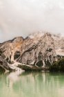 Amazing view of Dolomites mountain range with green lake water reflecting rough rocky slopes covered with fog and clouds in Italy — Stock Photo