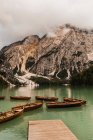 Amazing view of Dolomites mountain range with green lake water reflecting rough rocky slopes covered with fog and clouds in Italy — Stock Photo
