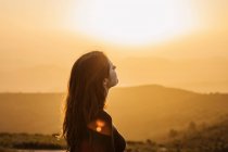 Seitenansicht einer glücklichen Frau, die mit geschlossenen Augen auf einem Hügel steht und die Freiheit genießt, während sie die bergige Landschaft bei Sonnenuntergang bewundert — Stockfoto