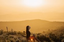 Side view of peaceful female traveler sitting on hill with closed eyes and enjoying nature in highlands at sundown — Stock Photo