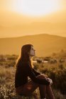 Vista lateral do viajante feminino tranquilo sentado na colina com os olhos fechados e desfrutando da natureza nas terras altas ao pôr do sol — Fotografia de Stock