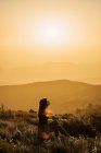 Vista laterale di tranquillo viaggiatore femminile seduto sulla collina con gli occhi chiusi e godersi la natura negli altopiani al tramonto — Foto stock