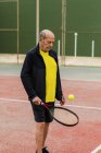 Deportista senior rebotando pelota en raqueta mientras se prepara para el partido de tenis en la cancha - foto de stock