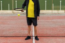 Crop deportista senior rebotando pelota en raqueta mientras se prepara para el partido de tenis en la cancha - foto de stock