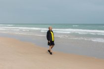 Пожилой спортсмен прогуливается по пляжу рядом с морем во время тренировки летом — стоковое фото