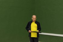 Sportif âgé avec balle de tennis et raquette regardant vers le bas tout en se tenant contre le mur vert pendant l'entraînement dans la salle de gym — Photo de stock