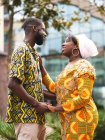 Side view of cheerful black couple in bright outfit with ornament embracing while standing on urban pavement and looking at each other — Stock Photo