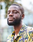 Pensativo não barbeado afro-americano macho em camisa ornamental olhando para a câmera enquanto em pé na cidade de verão — Fotografia de Stock