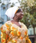 Vista lateral de la alegre joven africana en ropa brillante con adorno floral mirando hacia otro lado de pie en la ciudad - foto de stock