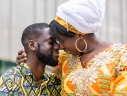 Cheerful African woman in traditional wear sitting close to unshaven boyfriend in ornamental clothes on city bench — Stock Photo