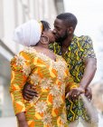 Етнічний чоловік із закритими очима обіймає і цілує жінку-партнера в яскравому традиційному одязі з орнаментом у місті — стокове фото
