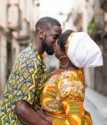 Side view of black couple in bright outfit with ornament embracing and kissing while standing on urban pavement with eyes closed — Stock Photo