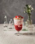 Verre de baies sucrées savoureuses et crème glacée délicieuse garnie de noix et de fraises servies sur la table près de bocaux en verre — Photo de stock