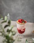 Vaso de sabrosas bayas dulces y delicioso helado adornado con nueces y fresas servidas en la mesa cerca de frascos de vidrio - foto de stock