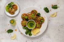 Top view gustose frittelle alle erbe appetitose guarnite con salsa verde sana prezzemolo e fette di limone sul tavolo bianco — Foto stock