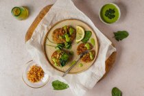 Composición vista superior de apetitosos buñuelos de hierbas con salsa verde y rodaja de limón servidos en tablero de madera y papel artesanal - foto de stock
