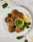 Top view yummy appetizing herbal fritters garnished with healthy green sauce parsley and lemon slices on white table — Stock Photo