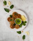 Top view yummy appetizing herbal fritters garnished with healthy green sauce parsley and lemon slices on white table — Stock Photo