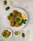 Vista superior deliciosos buñuelos de hierbas apetitosos adornados con perejil salsa verde saludable y rodajas de limón en la mesa blanca - foto de stock