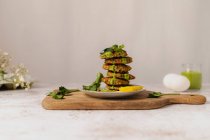 Fresh tasty herbal fritters stacked on plate and decorated with green sauce and lemon slice served on wooden cutting board — Stock Photo