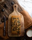 Composição da vista superior do pão cozido na hora inteiro colocado na placa de corte de madeira perto da faca e da xícara de leite — Fotografia de Stock