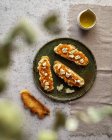 Вид зверху апетитні свіжі тости з джемом і козячим сиром, подані на тарілці біля глечика з органічною оливковою олією — стокове фото
