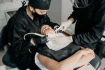 Сверху стоматологи с зубной дрелью и шприцем с воздушной водой делают лечение зубов для клиента в современной клинике — стоковое фото