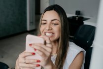 Patientin mit weißen Zähnen sitzt nach der Behandlung in der Klinik auf dem Zahnarztstuhl und porträtiert sich auf dem Smartphone — Stockfoto