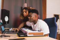Side view of young African American partners using netbook with sound recording software on screen in music studio — Stock Photo