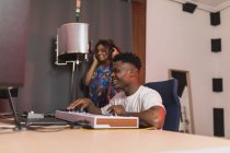 Сторона зору молодих афроамериканських партнерів за допомогою нетбука з програмним забезпеченням запису звуку на екрані в музичній студії — стокове фото