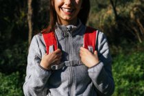 Anonymous happy optimistic young female hiker in activewear with backpack enjoying journey in green forest in sunny day — Stock Photo