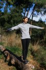 Повне тіло щасливої молодої жінки в спортивному одязі балансує на стовбурі падіння дерева під час прогулянок по зеленому лісу в сонячний день — стокове фото