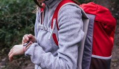 Vista laterale di crop female in activewear con zaino utilizzando GPS sul fitness tracker per la navigazione durante le escursioni nella foresta — Foto stock