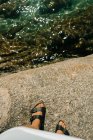 Крупним планом жіночі босоніжки на деяких каменях і в морі нижче — стокове фото