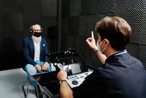 Älterer Mann mit Kopfhörer und Maske sitzt im Zimmer mit einem Arzt, der audiologische Hördiagnostik durchführt — Stockfoto