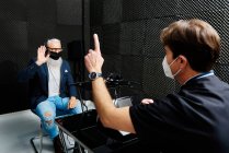 Hombre de edad avanzada en auriculares y máscara sentado en la habitación con el médico que realiza el diagnóstico audiológico de la audición - foto de stock