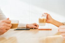 Vista lateral do casal adulto irreconhecível cortado sentado no balcão na cozinha e desfrutando de café aromático enquanto toma café da manhã em casa — Fotografia de Stock
