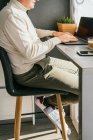 Vista lateral de corte irreconhecível macho de meia-idade trabalhando no balcão com netbook e xícara de café na cozinha pela manhã — Fotografia de Stock