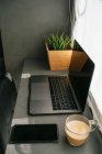 Сучасний ноутбук і смартфон, розміщені на лічильнику з чашкою ранкової кави на кухні, освітленій сонячним світлом — стокове фото