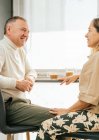 Side view of content adult couple sitting at counter in kitchen and enjoying aromatic coffee while having breakfast and looking at each other — Stock Photo